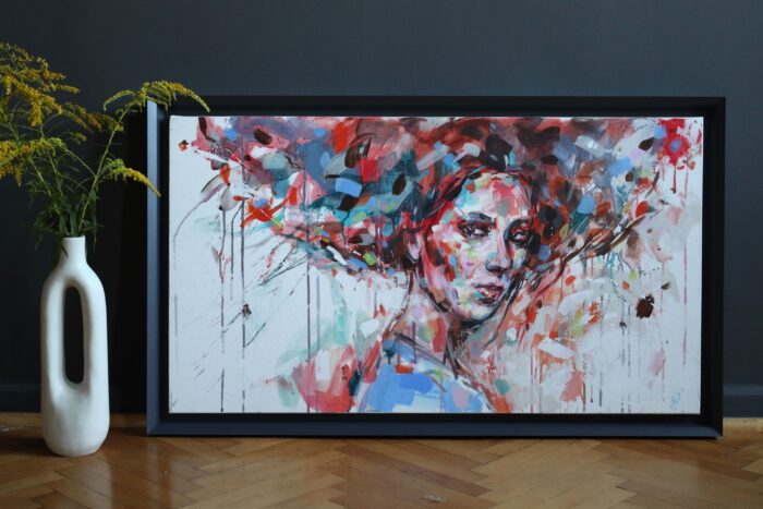 Abstrakcyjny portret kobiety. Obraz ręcznie malowany na płótnie. Autor Małgorzata Sęk. Obok obrazu stoi wazon.