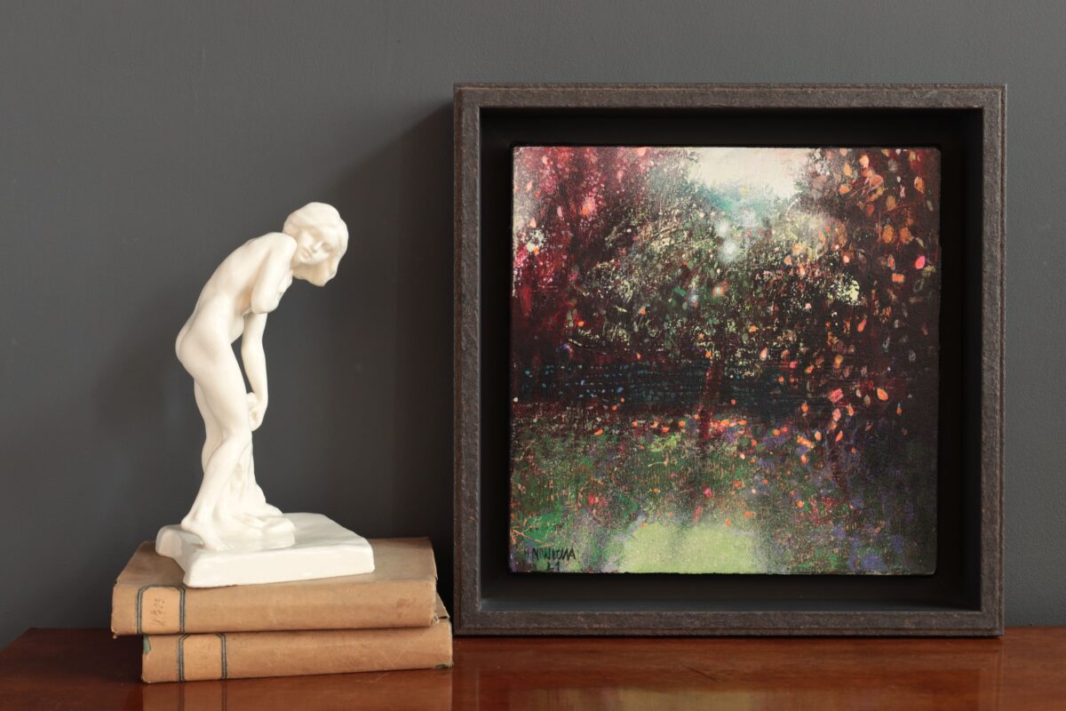 Mały obraz impresjonistyczny przedstawia ogród. Autor Halina Nowicka. Obok obrazu stoi mała figurka.
